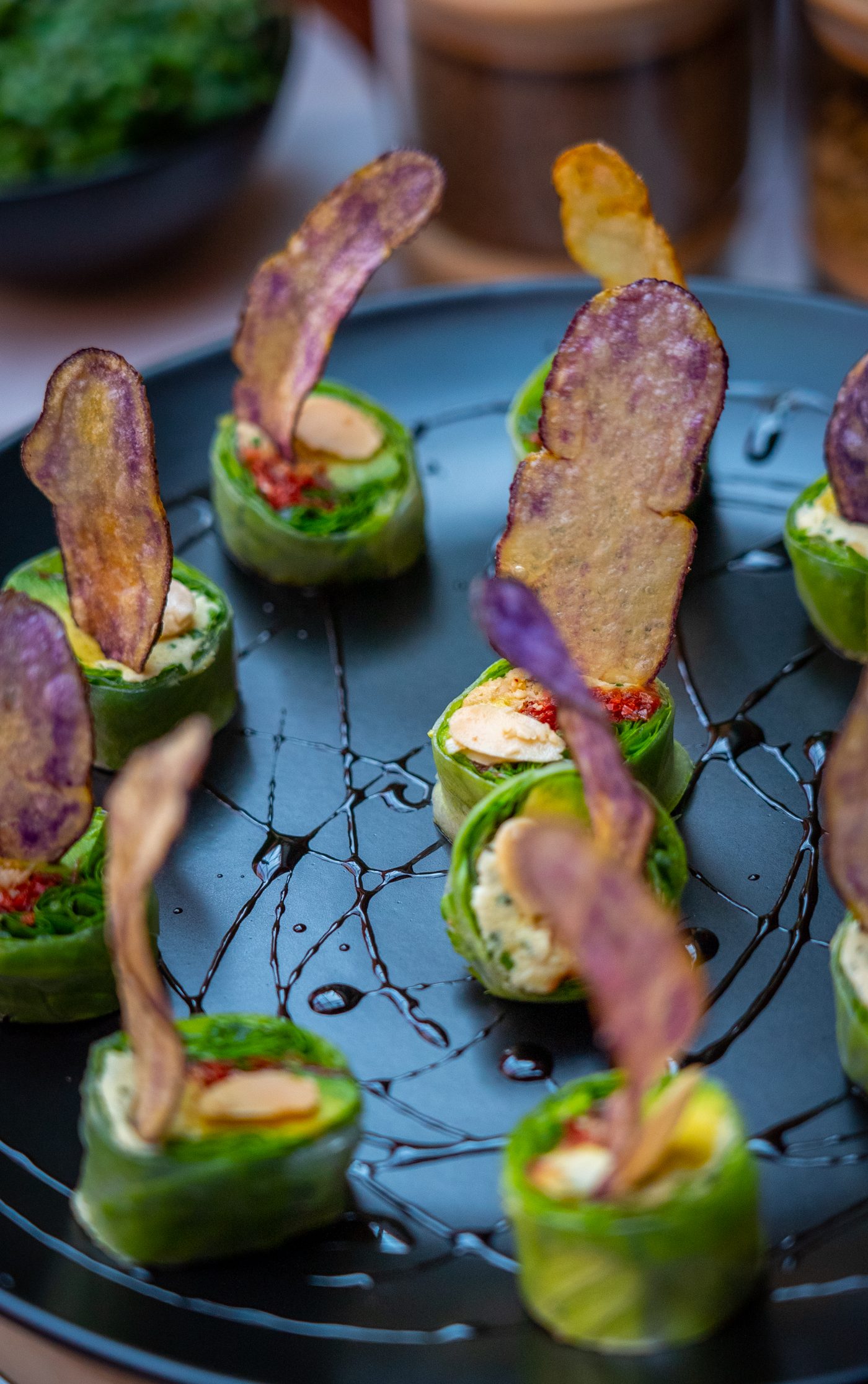 Rollitos verdes con crema, almendras y chips de papa nativa sobre plato oscuro